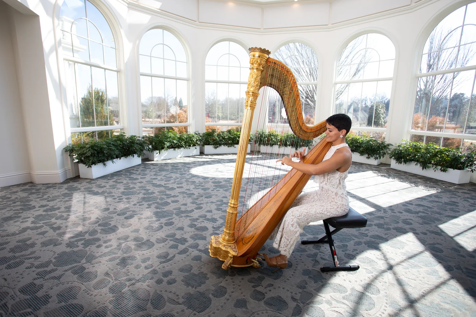 Victoria Greer playing her harp in a sunlit ballroom